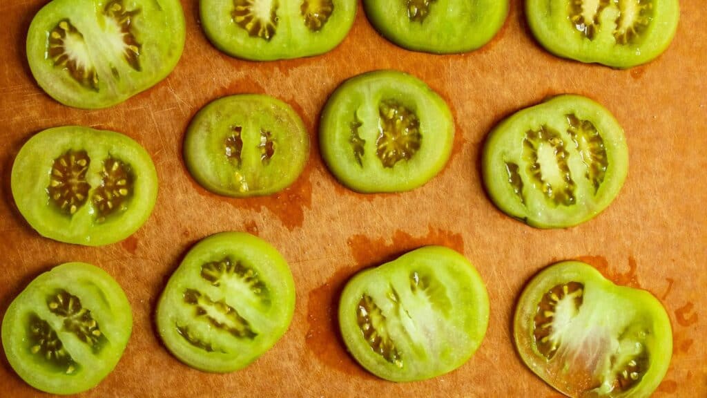 Sliced green tomatoes on a brown cutting board.