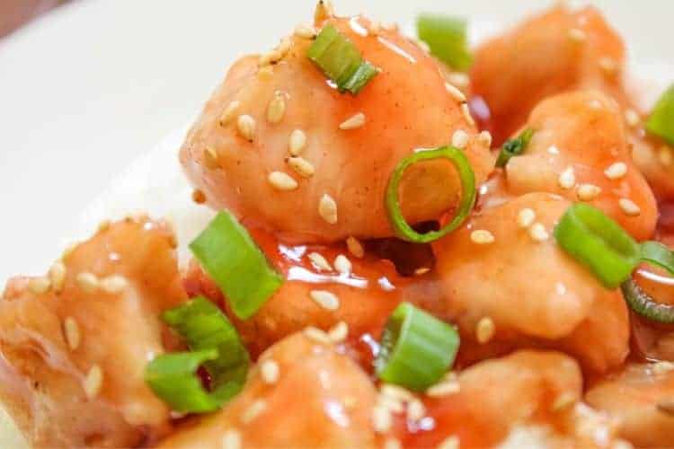 Closeup of sweet and sour chicken with sesame seeds and green onions on top on a white plate