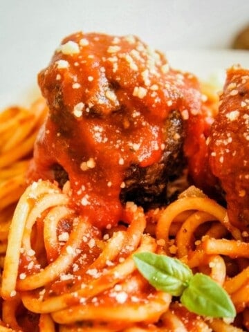 Spaghetti with meatballs on top covered in sauce. Basil piece in front.