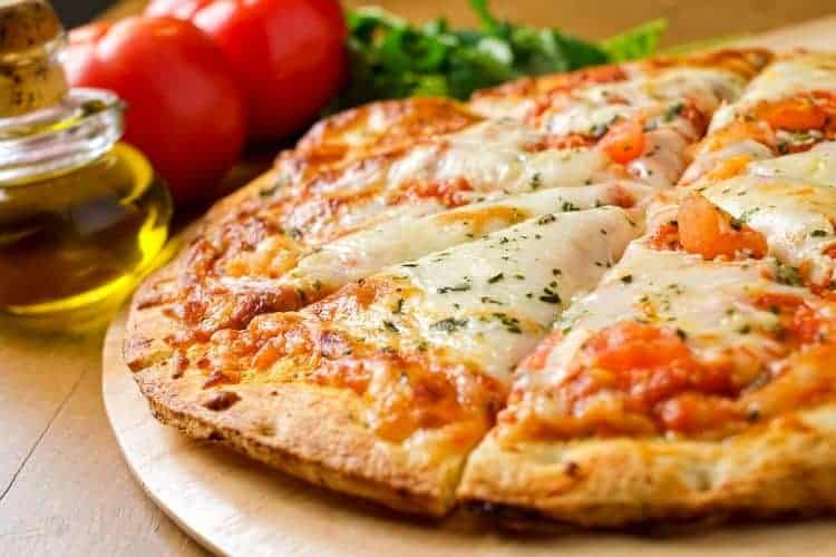 Full pizza cut into slices with olive oil, tomatoes, and basil in the background