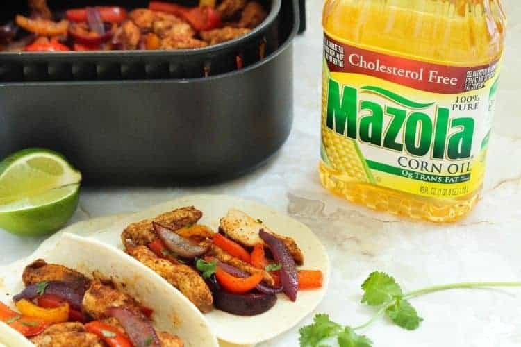 Air Fryer Chicken Fajitas inside tacos with air fryer basket and Mazola Corn Oil bottle in background from side angle