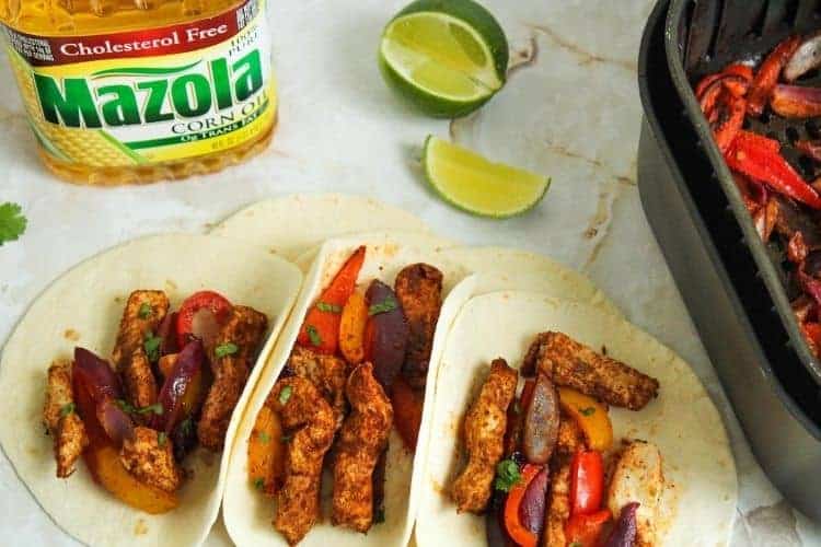 Air Fryer Fajitas inside tortillas with air fryer basket, lime wedges, and Mazola Corn Oil bottle in background