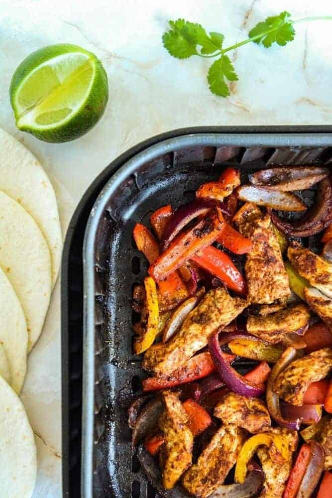 Air Fryer Fajitas inside air fryer with tortillas and lime wedges peeking out of the edges of photo