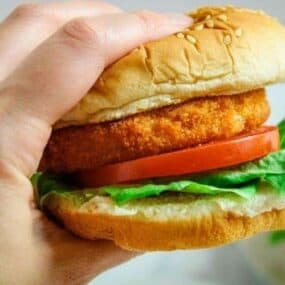 Air Fryer Chicken Patty sandwich being held in a hand with lettuce and tomato.