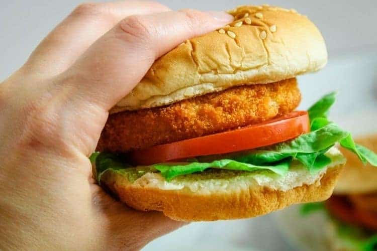 Air Fryer Chicken Patty sandwich being held in a hand with lettuce and tomato.