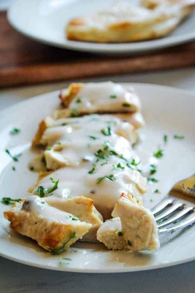 Air Fryer Turkey Cutlets covered in mushroom sauce sliced on a white plate with a fork in one piece