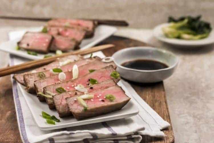 Sliced air fryer yellowfin tuna steaks on a white plate with chopsticks and sauce on the side