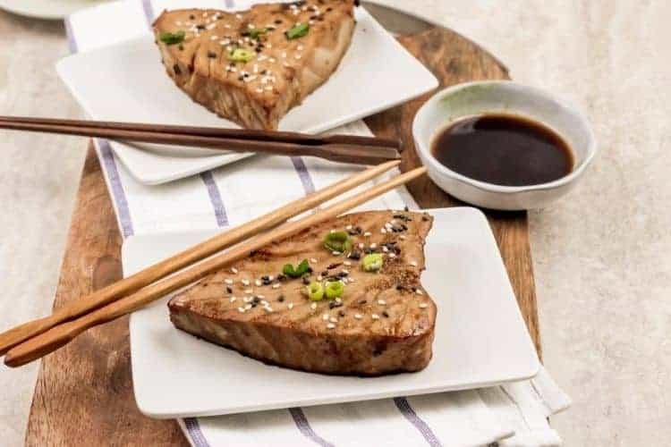 Cooked whole tuna steak on white plate with chopsticks and sauce