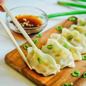 Instant Pot Pot Stickers on a cutting board with chopsticks about to pick up one