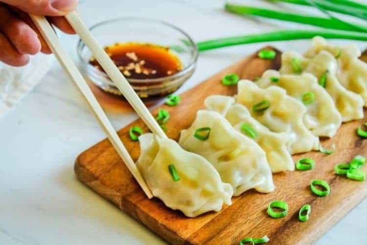 Instant Pot Pot Stickers on a cutting board with chopsticks about to pick  up one