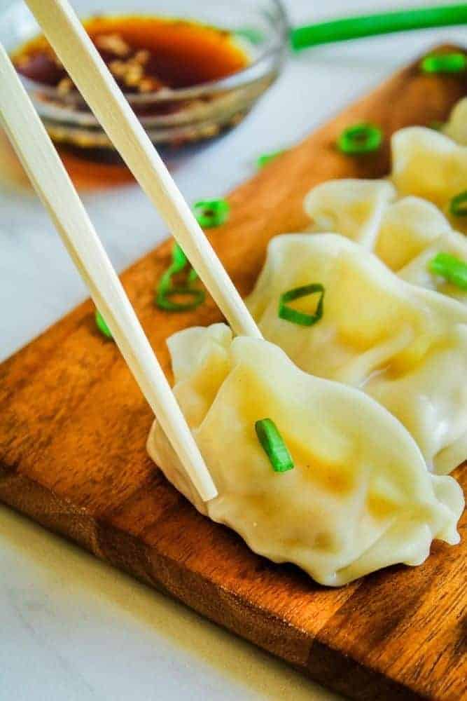 Potstickers on brown cutting board with chopsticks picking up one