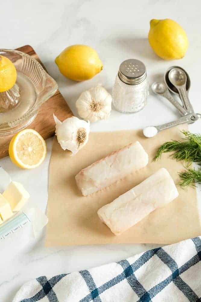 Raw cod on a cutting board with garlic, lemon, dill
