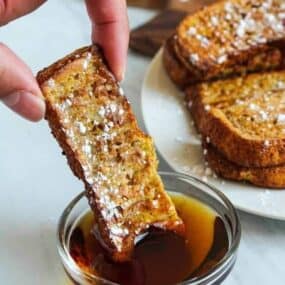 Air Fryer French Toast Stick being dipped into maple syrup