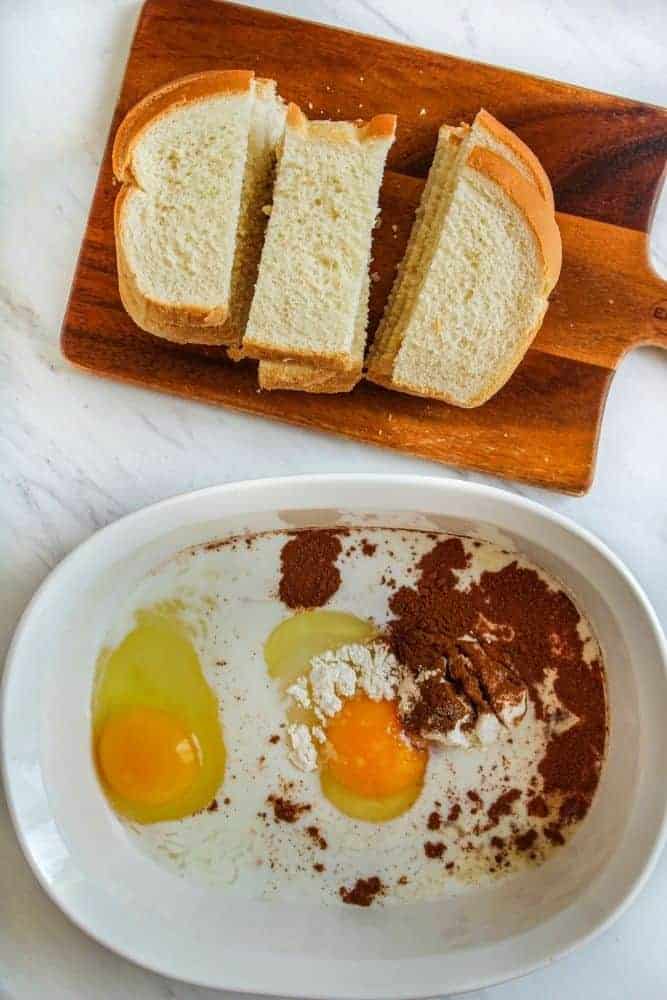 Bread cut into thirds on a cutting board with a bowl of all other ingredients underneath