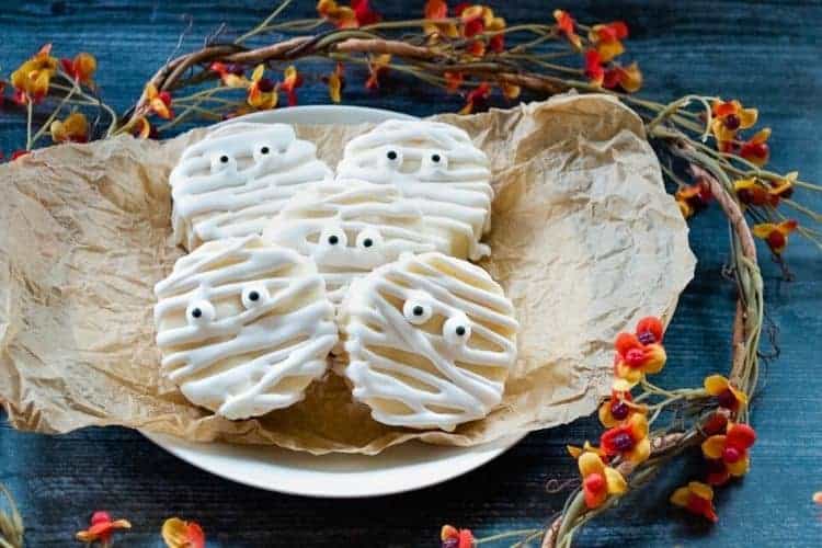 No-Bake Easy Halloween Mummies on a white plate with brown paper surrounded by fall foliage