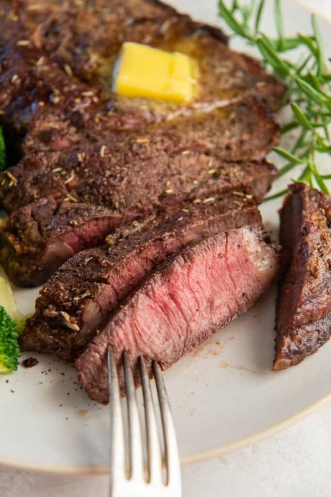 Sliced cook ribeye steak on plate with a fork in a bite