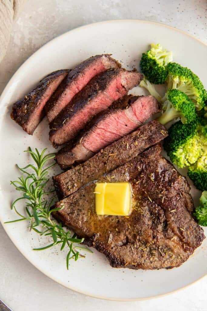 Air Fryer Frozen Steak cooked on a plate and cut with butter on top.