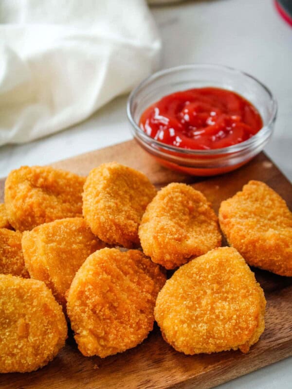 Air Fryer Chicken Nuggets on a brown cutting board with a little bowl of ketchup