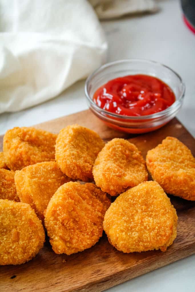 Air Fryer Chicken Nuggets on a brown cutting board with a little bowl of ketchup