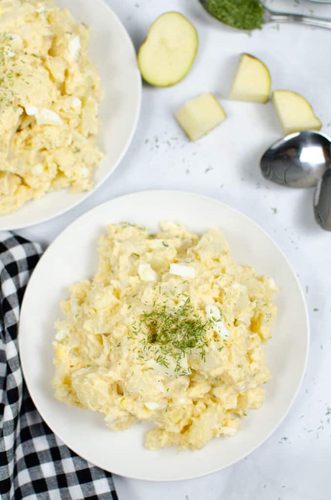 Instant Pot Potato Salad on a white plate with garnish on top and a black and white plaid napkin to side