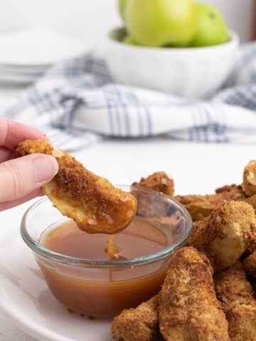 Air Fryer Apple Slices being dipped in caramel sauce on a white plate