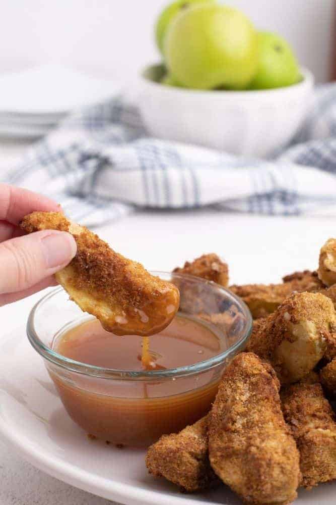 Air Fryer Apple Slices being dipped in caramel sauce on a white plate