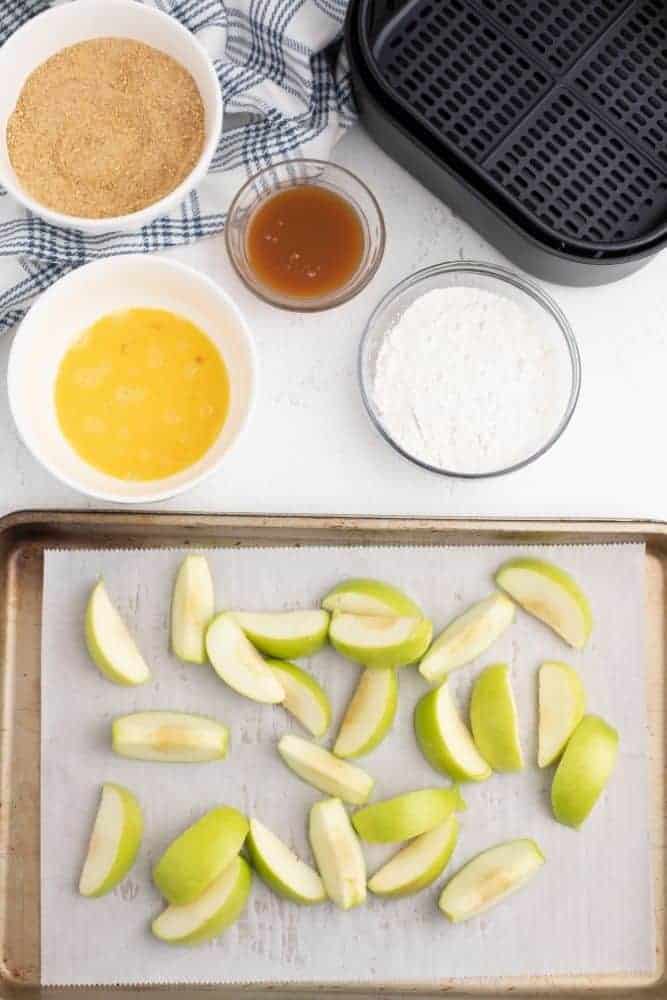 Apples sliced on a bakign sheet with other ingredients in bowls