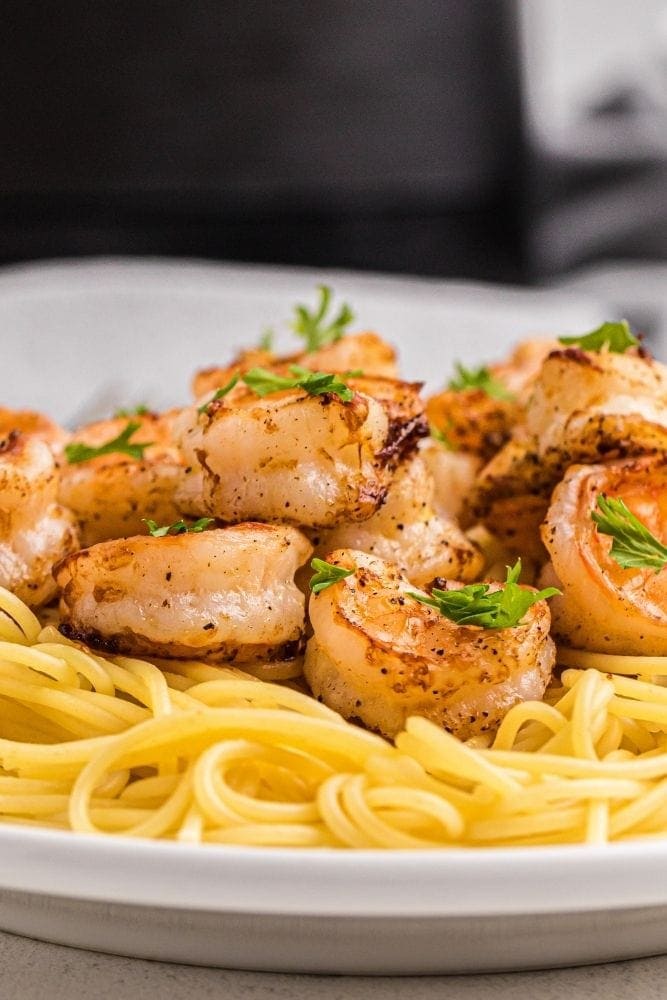 Air Fryer Shrimp on top of pasta on white plate from side angle