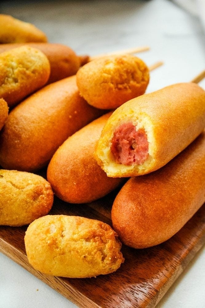 Corn Dogs and Mini Corn Dogs on a brown platter with once corn dog bitten into