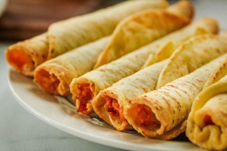 Air Fryer Taquitos in a line on a white plate