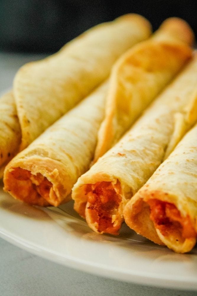 Closeup of air fryer taquitos in a portrait style image on a white plate