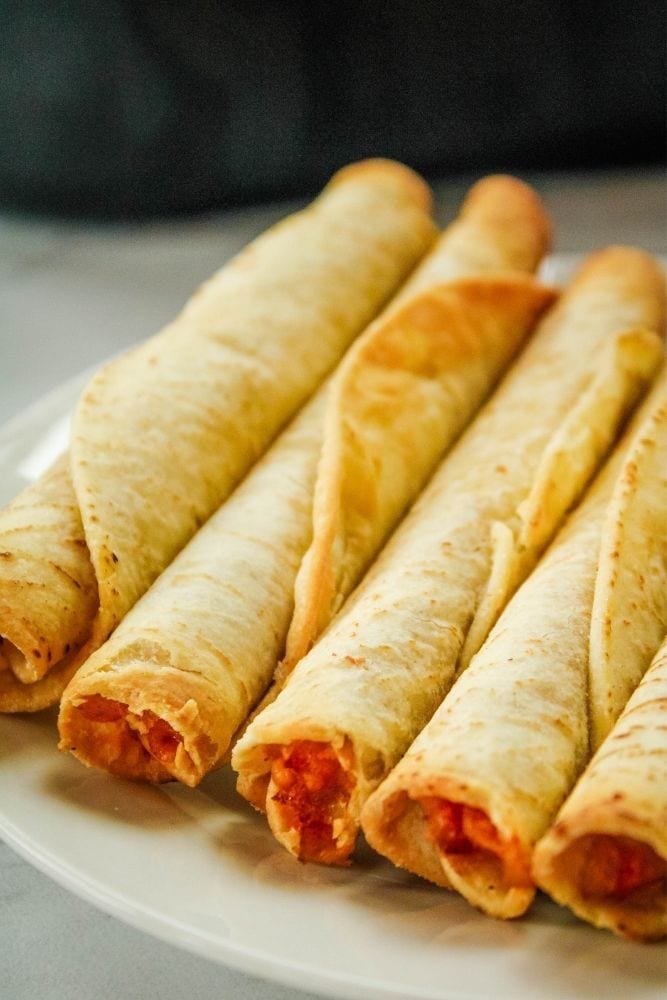 Cooked air fryer taquitos in a line on a white plate