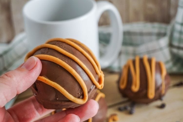 Hot cocoa bomb with peanut butter in hand with mug in background