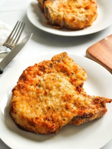 Air Fryer Bone-in Pork Chops on a white plate with fork and knife to the side