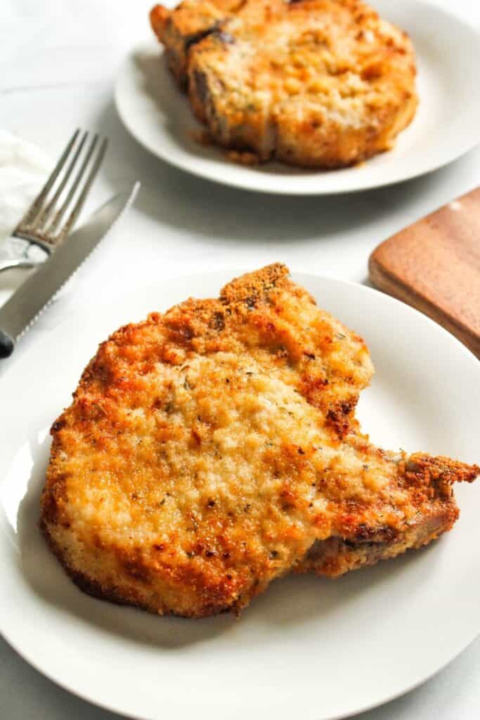 Air Fryer Bone-in Pork Chops on a white plate with fork and knife to the side