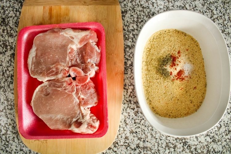 Raw pork chops in package next to white bowl of breadcrumbs and seasonings