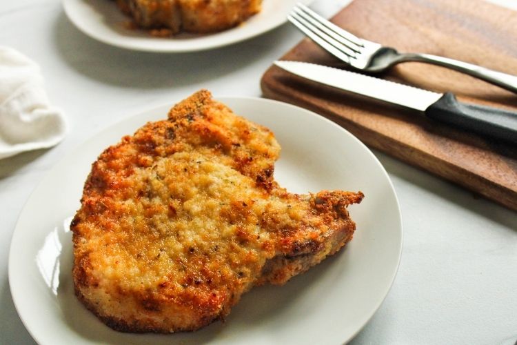 Air Fryer Breaded Pork Chop on a white plate next to a knife and fork