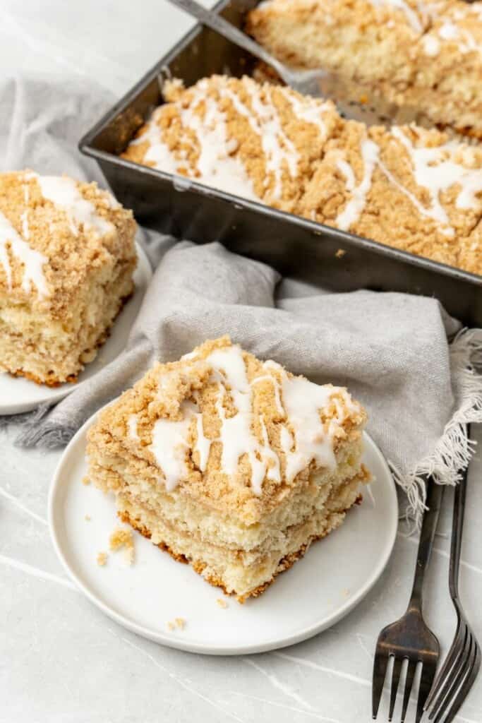 Slice of coffee cake on a plate with baking sheet full of it in background