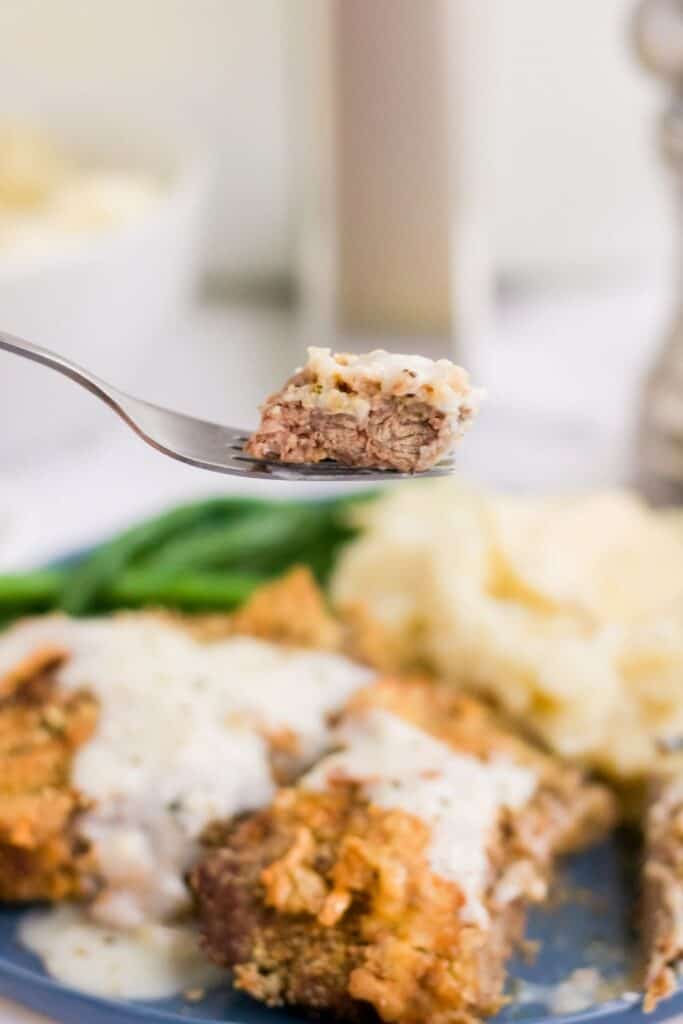 Country Fried Chicken with gravy on plate with a bite-sized piece on a fork above it
