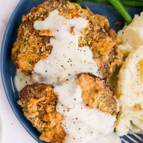 Air Fryer Chicken Fried Steak covered in gravy on a blue round plate with green beand and mashed potatoes