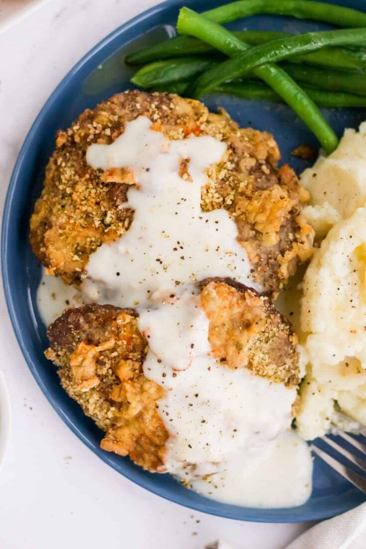 Air Fryer Chicken Fried Steak covered in gravy on a blue round plate with green beand and mashed potatoes