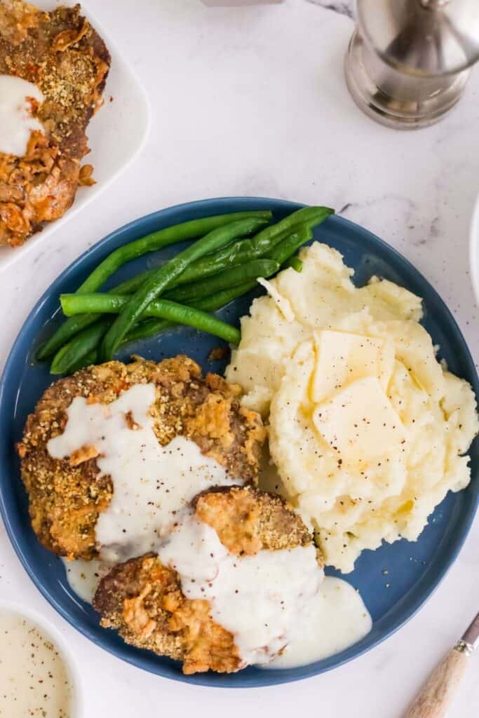 Air Fryer Country Fried Steak on a blue round plate with mashed potatoes and green beans