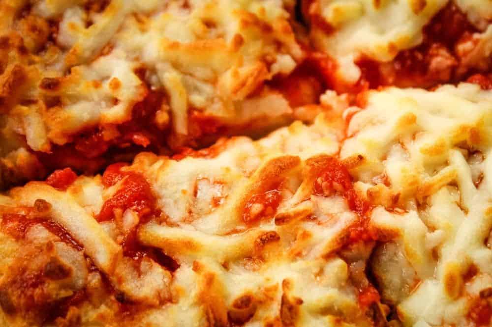 Closeup of cooked frozen pizza cut into slices with melted cheese and sauce