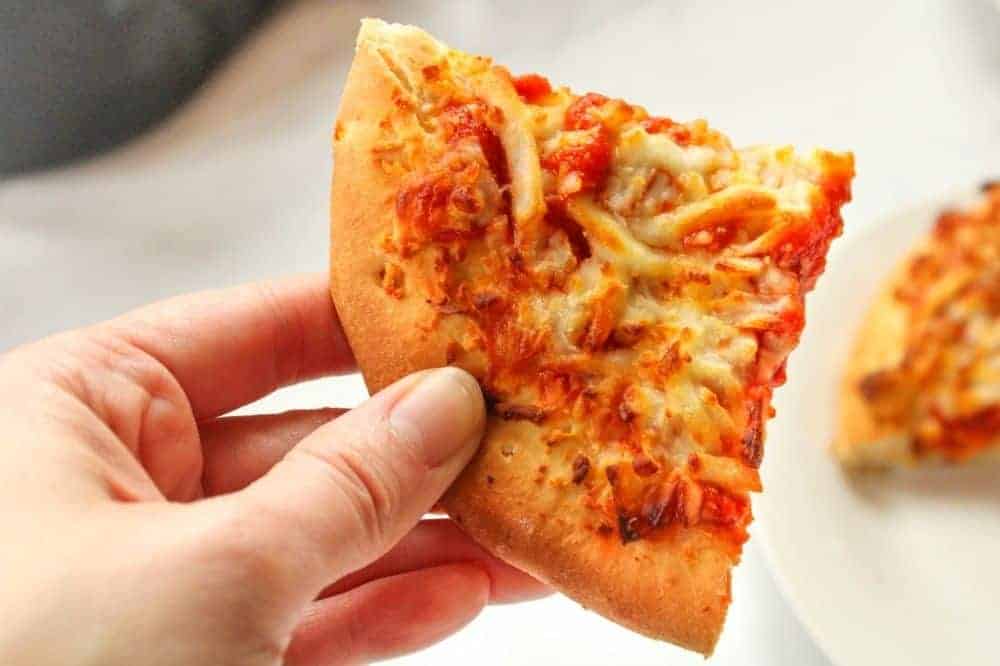 Hand holding a slice of frozen pizza in hand