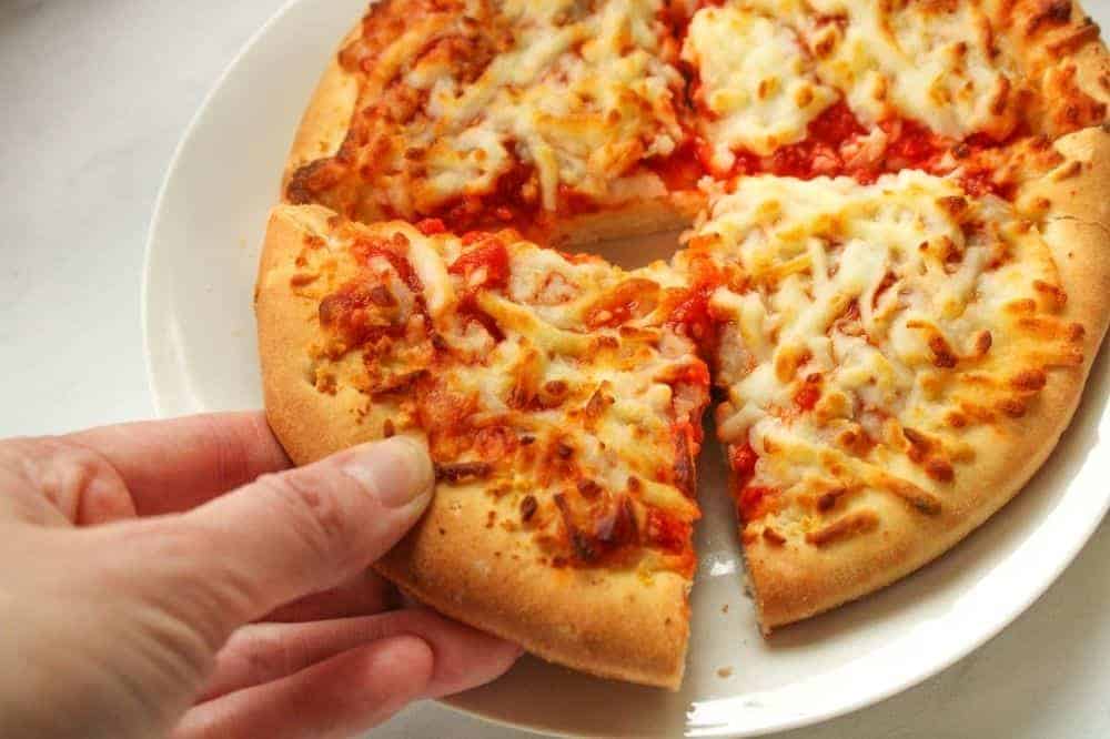 Hand grabbing a slice of pizza from an air fryer cooked personal mini pizza