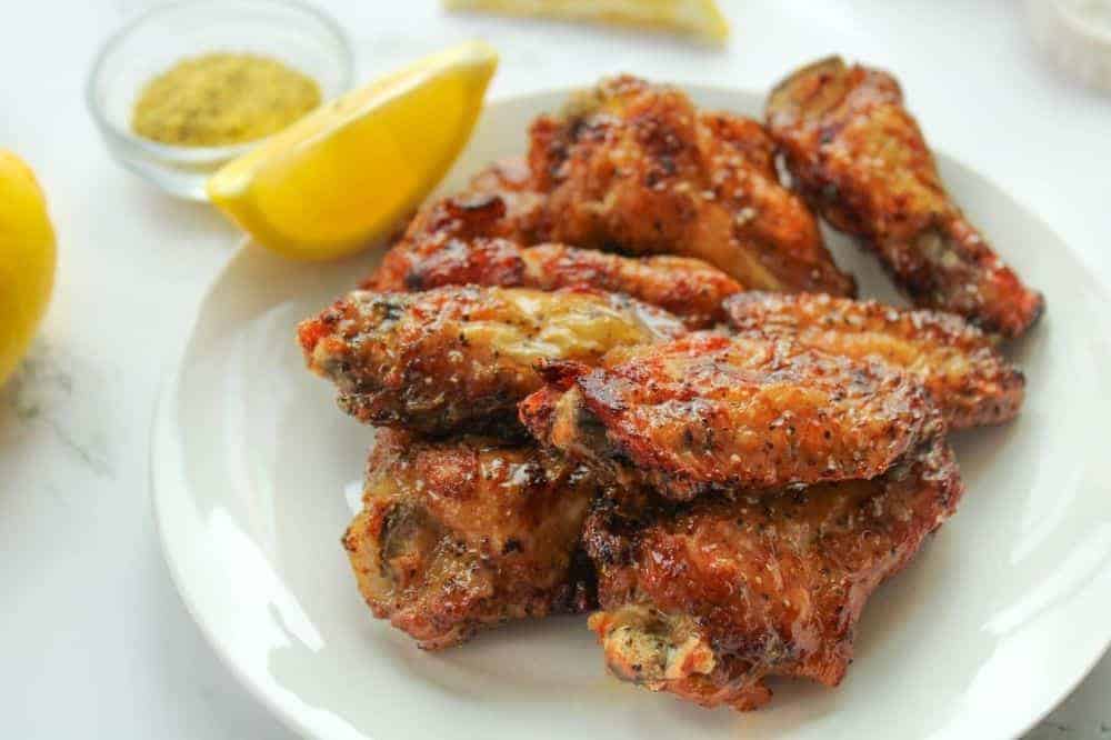 Lemon Pepper Chicken Wings on a white plate with lemon slice and lemon pepper seasoning in background