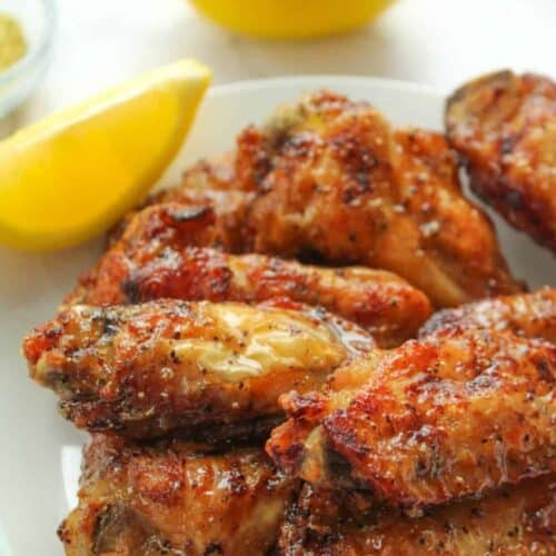 Lemon Pepper Air Fryer Wings on a white plate with a lemon slice and full lemon in the background