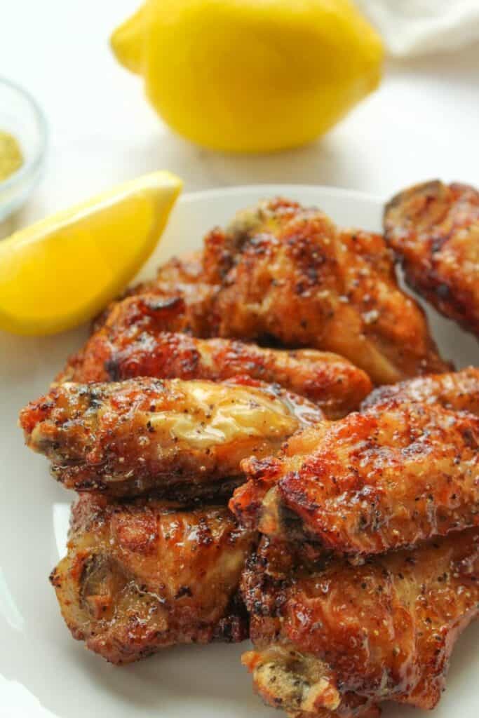 Lemon Pepper Air Fryer Wings on a white plate with a lemon slice and full lemon in the background