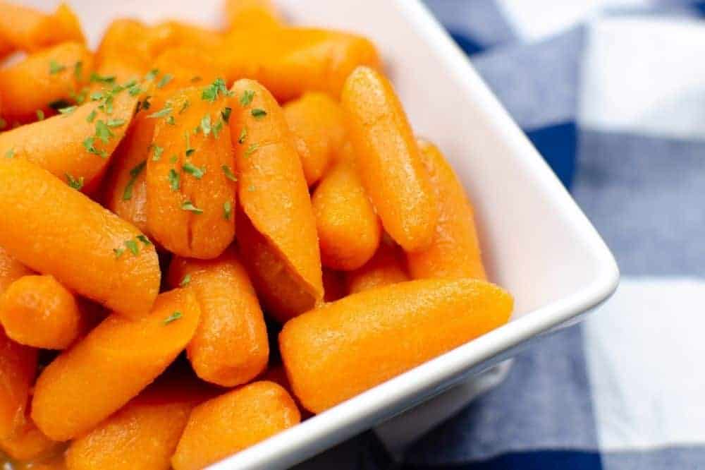 Closeup of cooked Instant Pot Carrots in a white square bowl with a white and blue checkered pattern tablecloth to the side