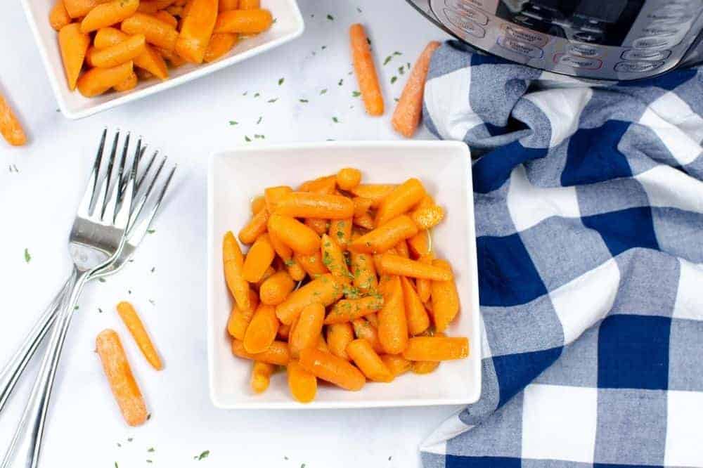 Instant Pot Carrots in a white square bowl with forks and a white and blue checkered tablecloth next to it